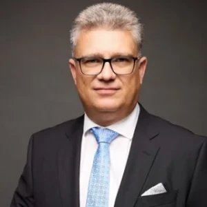 Porträt eines Anwalts der Kanzlei mit Brille, Anzug und hellblauer Krawatte.